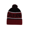 A red and black beanie features a pom-pom on top and decorative text. It includes a logo on the side.