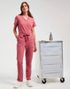 A woman wears pink cargo pants and a matching top, standing beside a mobile storage cart. The outfit features a drawstring waist.