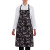 A black apron with a travel-themed pattern, featuring various design elements and a logo.