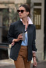 A woman is wearing a dark jacket with a light pink collar, holding a coffee cup in an outdoor setting.
