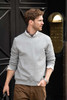 A grey unisex sweatshirt worn by a man, paired with a collared shirt and brown trousers, featuring a logo.