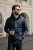 A man wearing a navy blue shell jacket with a hood, holding a coffee cup, and wearing sunglasses.
