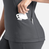 A grey banded V-neck top featuring side pockets, one holding a smartphone and the other a pen.