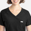 A black Y-neck top featuring a tuckable design and a chest pocket. The model has a smiling expression and short hair.