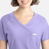 A lilac Y-neck top with a pocket and a logo, featuring a relaxed fit and short sleeves.