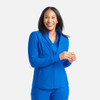 A woman wearing a bright blue full zip track jacket, smiling and holding her hands together. The jacket has a logo.