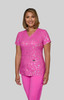 A pink scrub top featuring a floral print, worn by a model. The top has a V-neck and a logo on it.