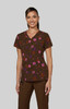 A woman models a brown floral scrubs top with pink and purple flowers, featuring a v-neck design.