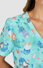 A short-sleeved top in a light teal with a playful animal print featuring cats and marine motifs. It has a branding logo.