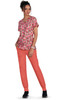 A woman in a floral pink top and coral jogger pants stands against a white background. The outfit features a logo.