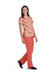 A woman wearing a colourful floral print top in shades of pink and orange, paired with coral pants and black shoes.