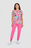 A woman stands in a colourful, patterned pink top and bright pink pants, with a light grey background.