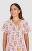 A pink scrub top with a playful print featuring drinks and fruit designs. The top has a V-neck and short sleeves.