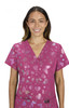 A woman wears a vibrant pink scrub top featuring a butterfly pattern and stars, with a logo on the chest.