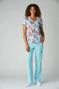 A stylish medical top featuring a colourful floral pattern, paired with light blue scrubs. The model stands smiling.