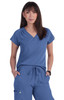 A blue scrub top with a V-neck and a pocket, worn by a model. The top features short sleeves and a relaxed fit.