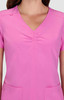 A pink scrub top featuring a V-neck and ruched detailing, with pockets at the front and a brand logo.