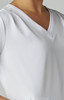A close-up of a white Sari Top featuring a V-neck design and textured fabric. It has a branding logo.