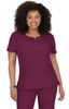 A woman wearing a short-sleeved scrub top in deep burgundy with a round neckline and pockets. The top has a logo.