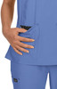A scrub top in light blue, featuring two front pockets with a contrasting black and white polka dot lining.
