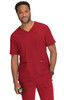 A man in a red scrub set stands smiling, holding a medical tool, with pockets on both the top and pants.