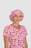 A pink bouffant cap with a heart print, worn by a model in a matching scrubs top with a heart design.