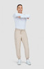 A model wearing beige joggers and a white long-sleeve shirt, smiling and posing against a plain background.