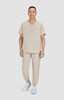 A model wearing beige scrubs with a v-neck top and jogger-style pants, paired with white sneakers.