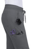 A pair of grey jogger pants featuring pockets, with scissors and pens visible. There is also a clip-on device attached.