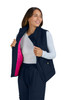 A woman wearing a navy blue vest, unzipped to reveal a bright pink interior, smiling while standing.
