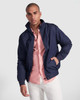 A navy waterproof jacket with a zip, featuring a collar and pockets, worn over a light pink shirt and white trousers.