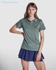 A women's polo shirt in a muted green colour with a logo, paired with a navy skirt.