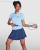 A woman models a light blue polo shirt and a navy skirt, holding a racket. The shirt features a logo.