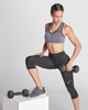 A cropped tank top in grey worn by a woman, paired with black fitness leggings, holding a dumbbell.