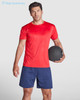 A red t-shirt featuring a logo, worn by a man holding a black exercise ball, paired with navy shorts.