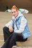 A light blue ladies' winter vest is worn over a white hoodie, paired with black trousers, seated on steps.