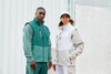 A green and grey softshell vest worn by two models, featuring a zippered front and a logo.