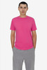 A model wearing a pink short sleeve fine jersey crew tee paired with grey trousers. The tee features a logo.