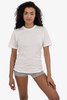 A woman stands wearing a white short sleeve fine jersey crew tee, styled with grey shorts. The shirt has a logo.