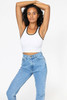 A woman poses wearing a white rib crop tank top with black trim, paired with high-waisted blue jeans.