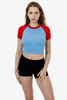 A short sleeve raglan tee in light blue with red sleeves, paired with black shorts. The model poses against a plain background.