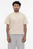 A short sleeve garment dye t-shirt in a beige colour, worn by a model with curly hair and grey pants.