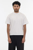 A short sleeve garment dye t-shirt in a light colour, featuring a logo, worn by a model standing against a plain background.