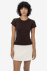 A brown cap sleeve baby tee displayed on a model, paired with a white skirt. The shirt has a subtle logo.