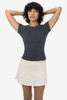A fitted cap sleeve baby tee in dark grey, paired with a light-coloured skirt. The model has curly hair and a neutral background.