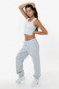 A model poses in grey heavy fleece sweatpants, paired with a cropped white tank top and white sneakers.