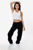 A model poses with one arm raised, wearing black heavy fleece sweatpants and a white crop top. The image features a logo.