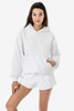 A white mineral wash fleece wide hoodie with a front pocket, styled with shorts and featuring a logo.