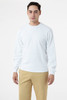 A man wearing a white crewneck sweater, styled with beige trousers. The sweater features long sleeves and has a logo.