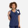 A navy mock wrap top with short sleeves, featuring a stethoscope and a tag, worn by a woman with curly hair.